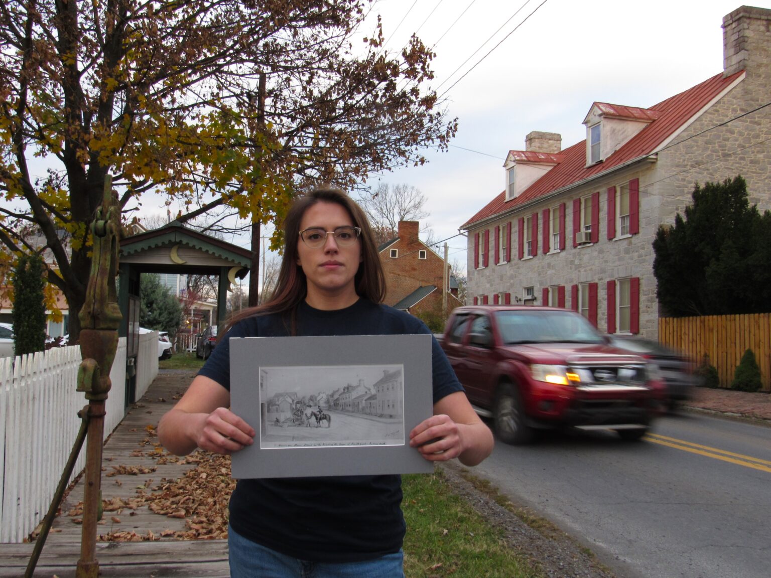 A woman stands in a village street holding a black-and-white photo of what the street used to look like.